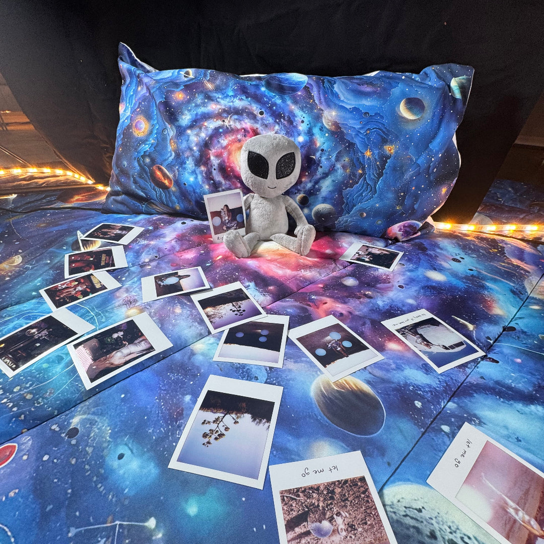 Space-themed bedding set with alien plush toy and photos on a bed.